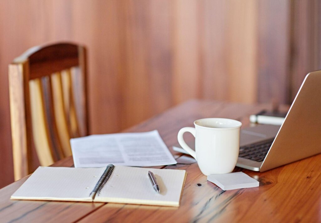 image of a table with a notebook, pen, laptop, post it pad, and coffee cup