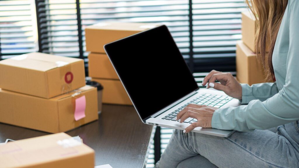woman with laptop on lap and shipping boxes in background
