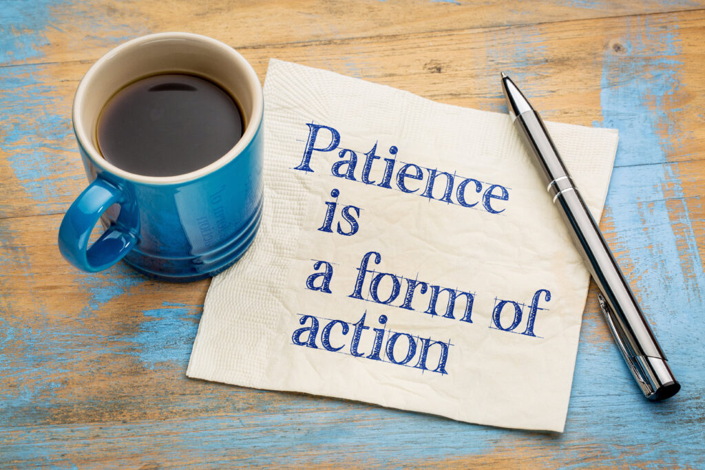 blue mug of coffee, silver pen, and words "patience is a form of action" printed on a napkin