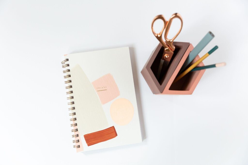 spiral-bound planner next to a pencil cup containing pencils and scissors
