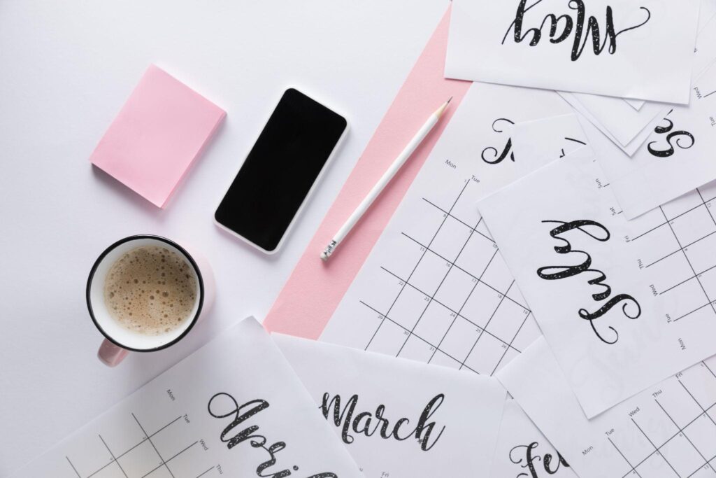 calendar pages, cell phone, pencil, pink post-it pad, cup of coffee