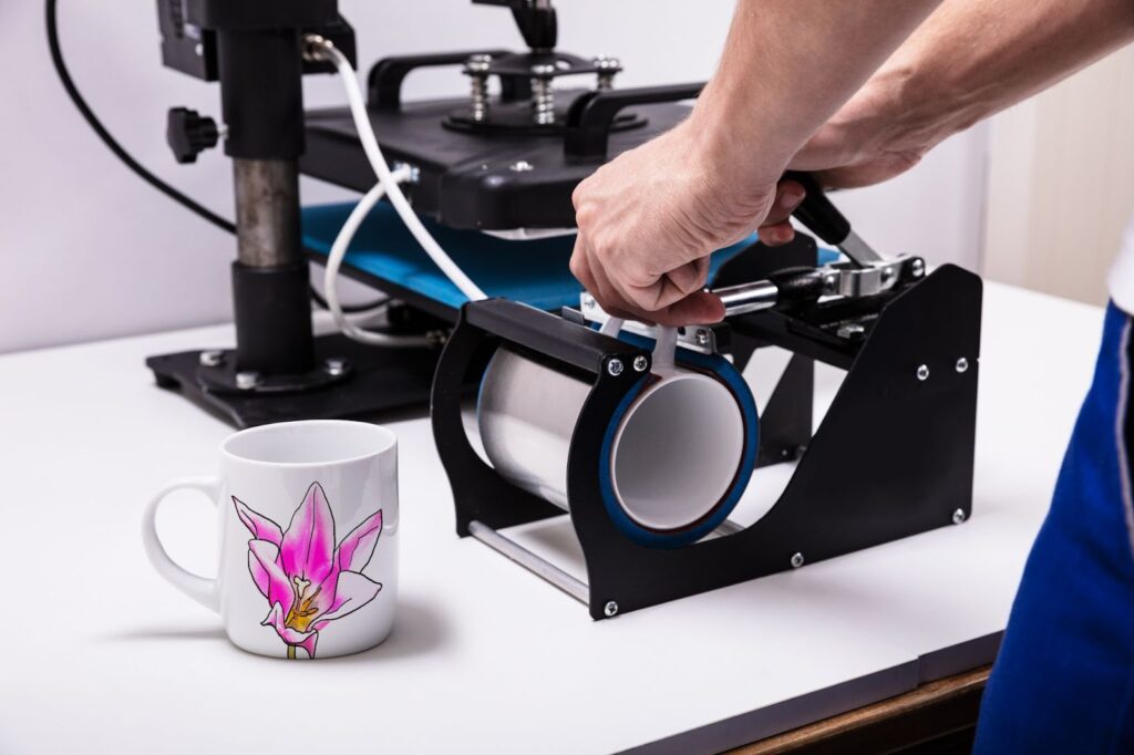 man operating a machine for screen printing designs on coffee mugs