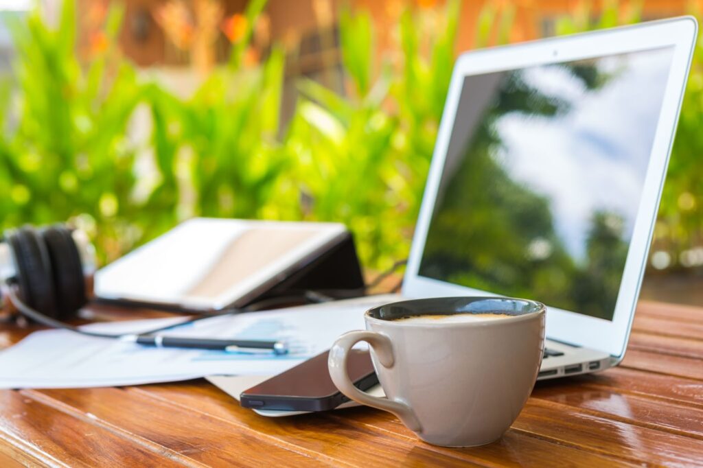 items on a table -- laptop, ipad, cell phone, headphones, notebook, pen, cup of coffee